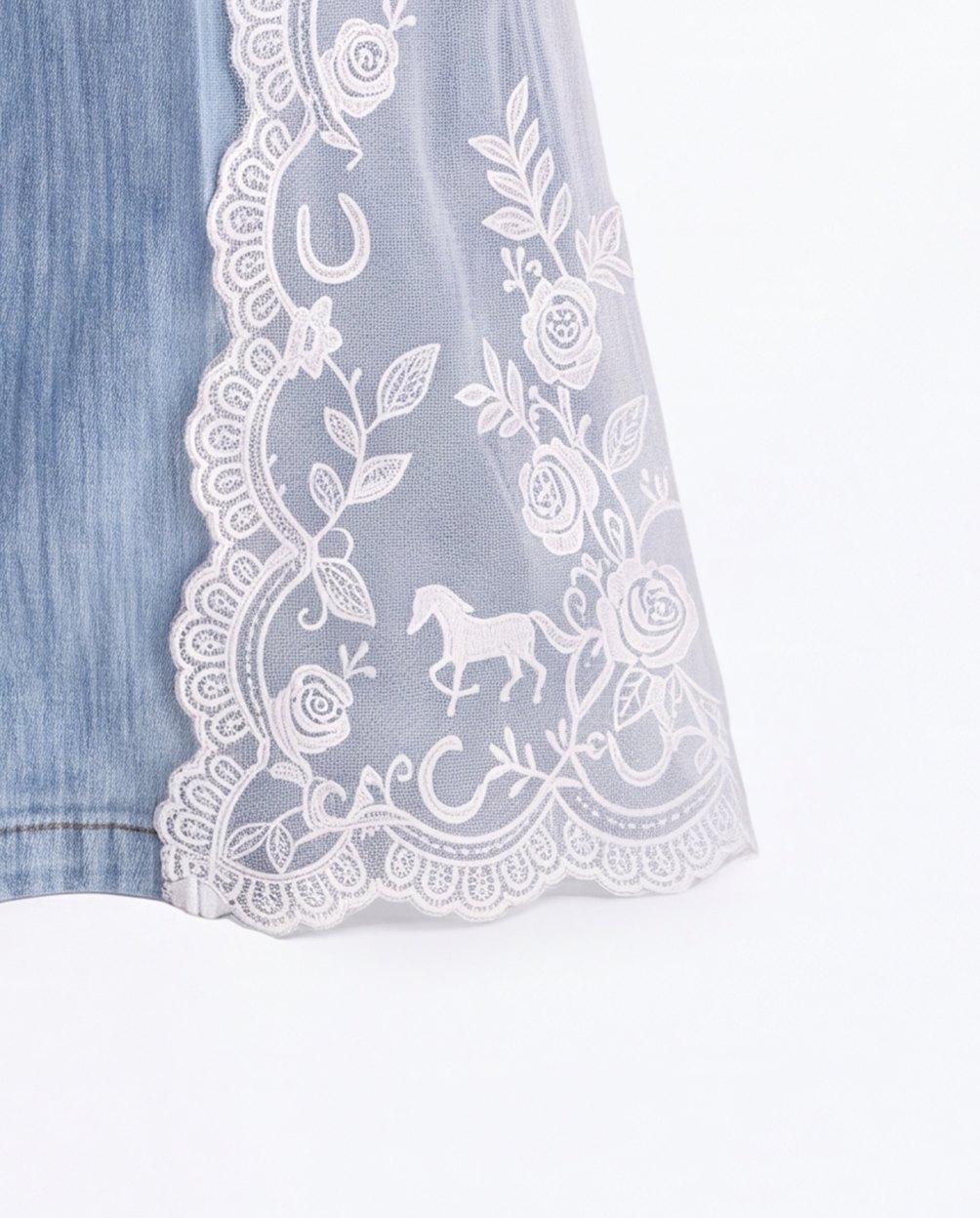 Close up of the sheer white lace at the hem, with horseshoes, roses and a small galloping horse